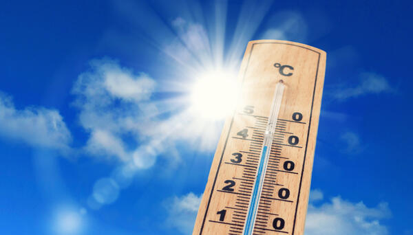 Ein Thermometer steht vor blauem Himmel und der Sonne, die hell scheint.