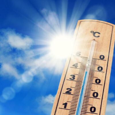 Ein Thermometer steht vor blauem Himmel und der Sonne, die hell scheint.