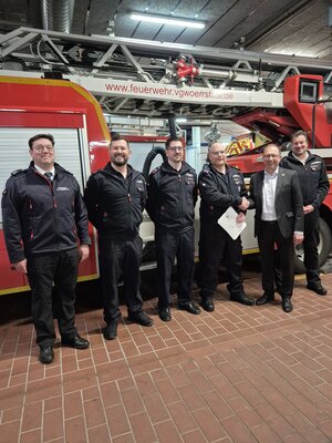 Bild vergr&ouml;&szlig;ern: Sechs M&auml;nner stehen vor einem Feuerwehrauto. Einer h&auml;lt eine Urkunde fest. Er hat eine neue Aufgabe bekommen.