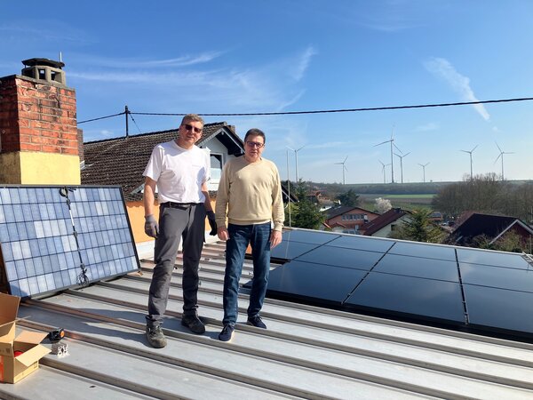 Zwei M&auml;nner stehen auf einem Dach. Dort ist eine Solaranlage. 