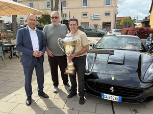 Bild vergr&ouml;&szlig;ern: Drei M&auml;nner stehen mit einem Pokal vor einem Auto.