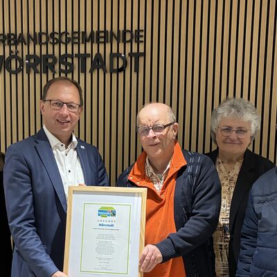 Zwei M&auml;nner halten eine Urkunde statt. Drei andere Leute stehen daneben.