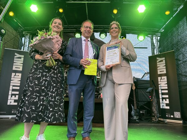 Auf einer B&uuml;hne stehen zwei Frauen und ein Mann. Sie er&ouml;ffnen zusammen ein Fest. 