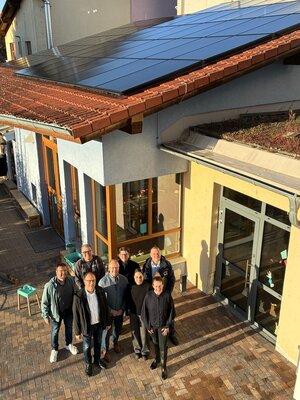 Bild vergr&ouml;&szlig;ern: Vor einem Geb&auml;ude stehen mehrere Menschen. Auf dem Dach sieht man eine neue Solaranlage. Die wird heute eingeweiht.