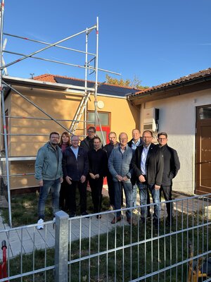 Bild vergr&ouml;&szlig;ern: Vor einem Geb&auml;ude stehen mehrere Menschen. Auf dem Dach sieht man eine neue Solaranlage. Die wird heute eingeweiht.