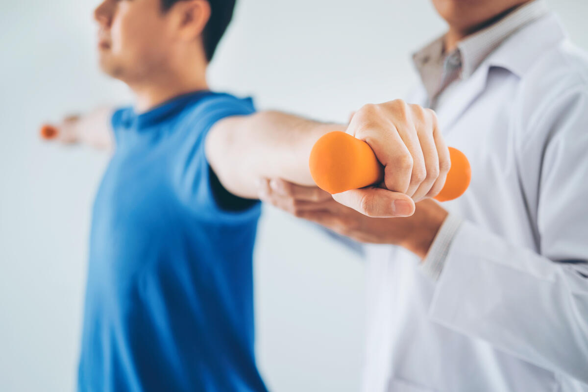 Ein Mann macht eine &Uuml;bung. Ein Physiotherapeut hilft ihm dabei.