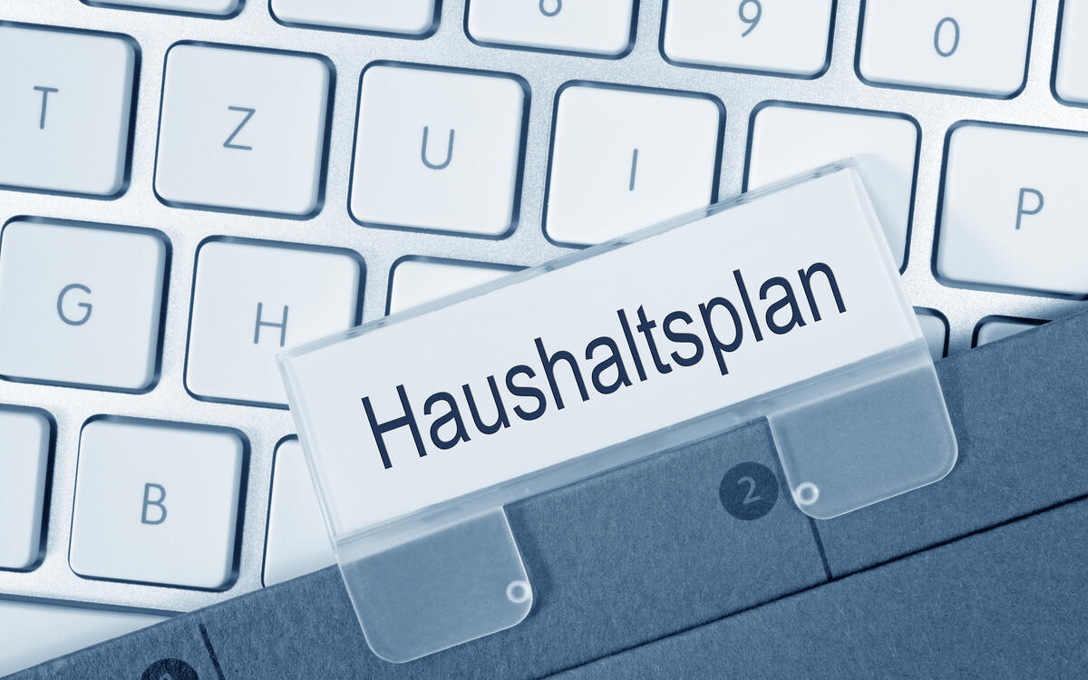 Eine Akte mit dem Haushaltsplan liegt auf einer Tastatur.